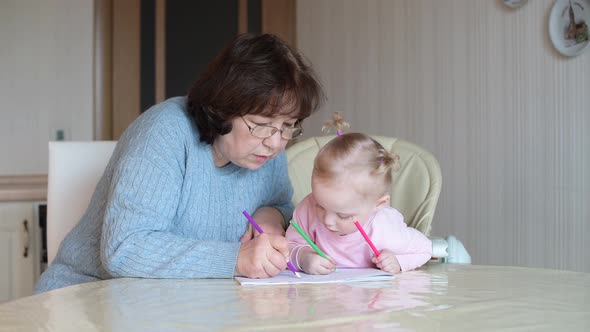 A little girl watches a nanny draw in an album. A child learns to draw alt