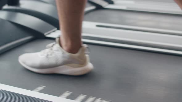 Young Asian guy feet in sneakers exercise running on treadmill fat burning workout in fitness class.