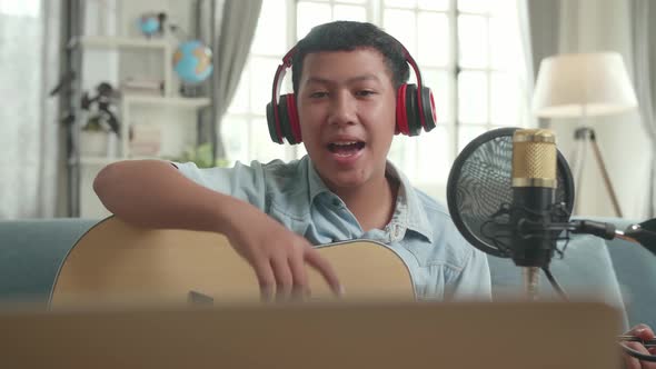 Asian Boy Vlogger With Guitar Looking And Read Comment On Computer Laptop alt