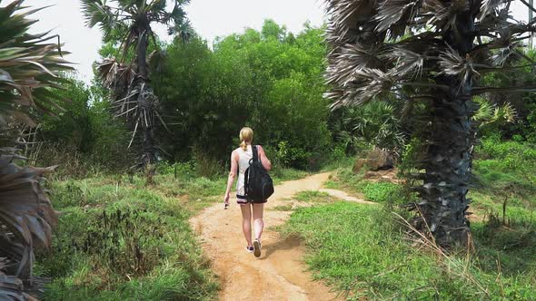 girl tourist with a backpack walking along a path in the forest of a tropical island alt
