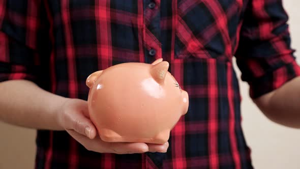 Woman Holds Piggy Bank on Palm and Throws Coin Inside alt