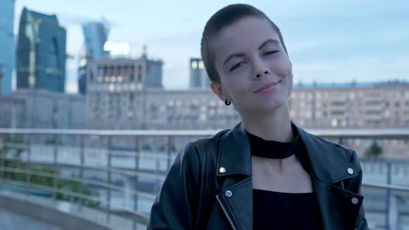 Young Attractive Stylish Woman with Short Shaved Hair Against Urban Background with Skyscrapers at alt