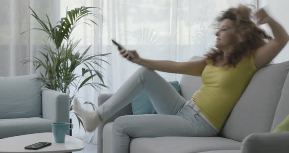 Woman sitting on the sofa and watching TV, she is holding the remote control