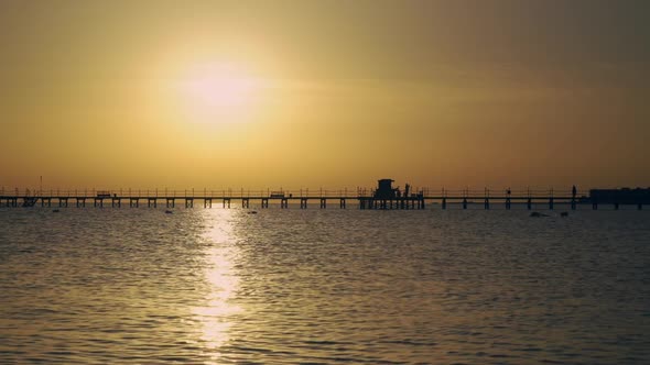 Sunrise in the Sea, People Are Walking Along the Pier alt