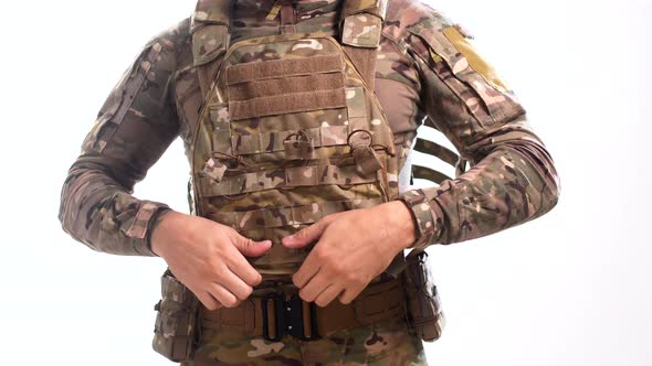 Man in combat camouflage is wearing a bulletproof vest over his head against a white background