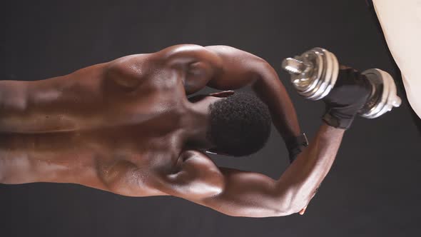 A Muscular AfricanAmerican Bodybuilder is Engaged with Dumbbells on an Isolated Dark Background alt