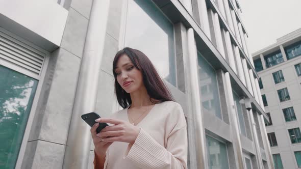 Young Beautiful Businesswoman Using Smartphone and Walking on City Streets of Downtown