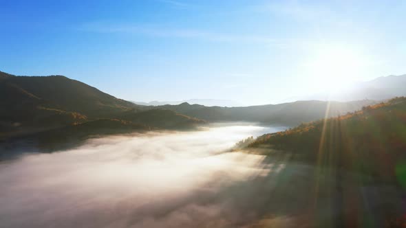 Sunrise Light Among Clouds Above Mountainous Canyon in Mist