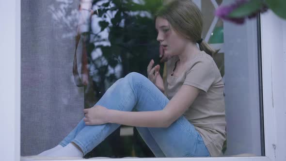 Desperate Scared Teenage Girl with Bruised Face Sitting on Windowsill with Unrecognizable Aggressive alt