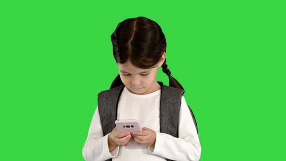 Concentrated School Girl with Backpack Typing on Her Pink Phone on a Green Screen Chroma Key alt
