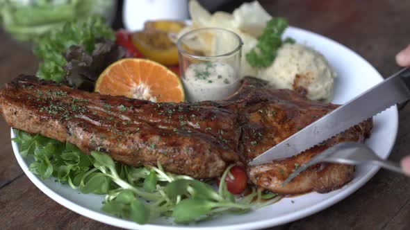 Cutting Pork T Bone With Knife And Fork Meat Fat And Bone Steak With Salad And Mashed Potato Sides