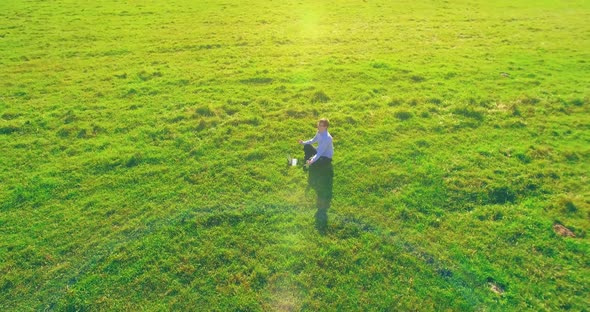 Low Orbital Flight Around Man on Green Grass with Notebook Pad at Yellow Rural Field alt