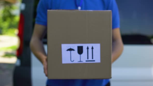Courier in Uniform Holds Box With Keep Dry, Fragile, This Way Up Signs, Service alt
