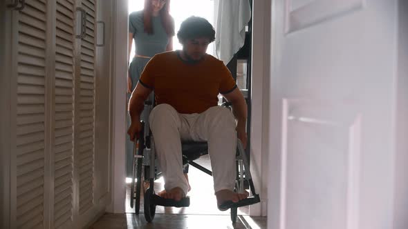 Man in a Wheelchair Trying to Pass the Hallway and His Wife Following Him alt