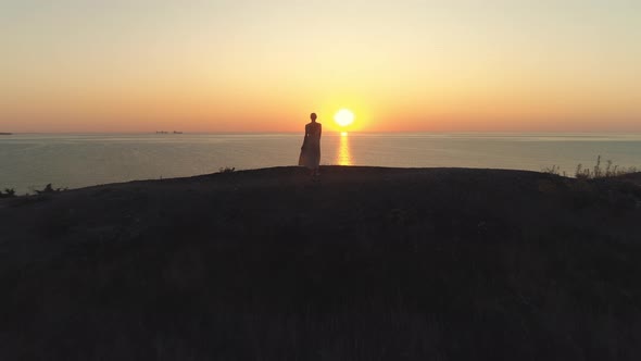 Woman Standing on Cliff Edge at Sunset Aerial View alt