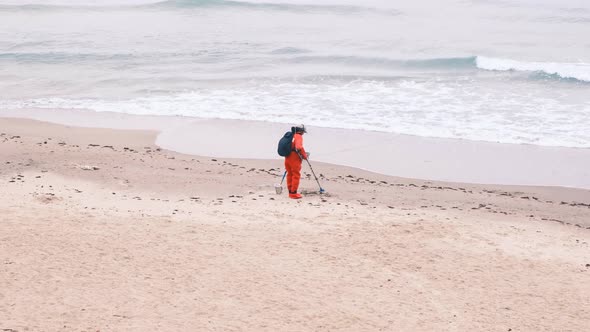 Man in Red Jumpsuit Looking for Lost Luxuries with Electronic Metal Detector on the Beach on a
