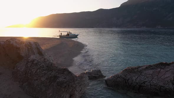 View of Wild Beach with Calm Sea Waves Boat and Mountains at Sunset alt