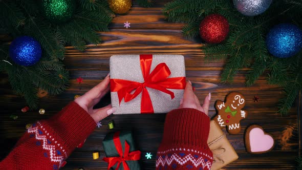 Hands puts gift wrapped in silver paper on wooden surface and then takes it.  alt