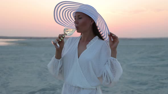 Elegant Woman with Glass of Wine Resting on Beach at Sunset