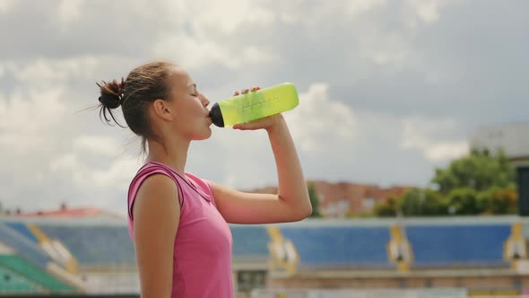 Girl Athlete Drinks Water at the Stadium alt