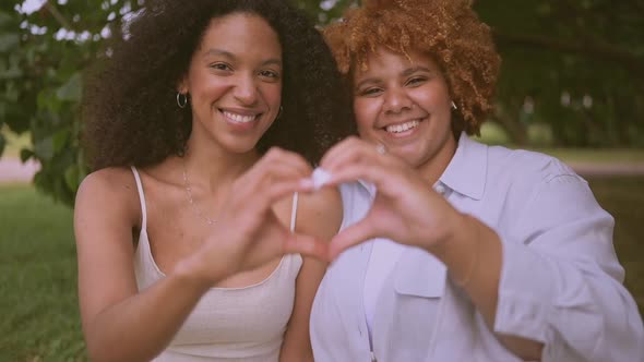 Young Beautiful Happy Lesbian African American Couple Sitting on Green Grass Showing Love Sign
