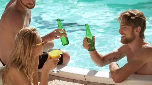 Two Smiling Caucasian Males in Pool Drinkin Beer with Blonde Female with Cocktail on Lounge alt