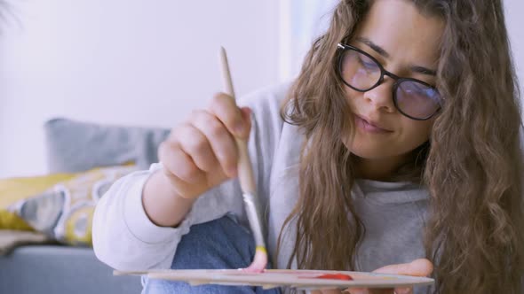 Positive Woman Takes White Paint From Tube to Draw Painting