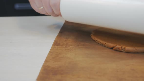Pastry Chef Baker Rolls Out Brown Dough on a Brown Rug on the Table with a Large White Rolling Pin