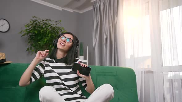 Woman in Earphones Sitting on Soft Couch at Home and Enjoying Modern Music alt