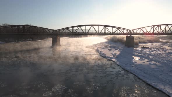 Drone Shot Flies Backward Over the Frozen River at Sunrise Car Driving on the Red Steel Bridge