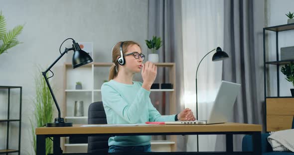 Female Freelancer in Glasses Sitting in front of Computer at Home and Holding Video meeting alt