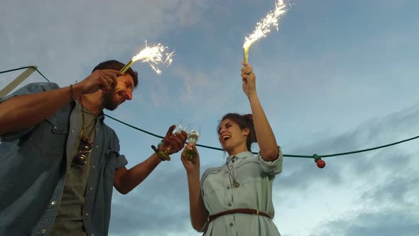 Low angle view of couple holding firework candles and toasting with champagne alt
