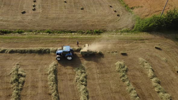 Farmer with Tractor Machine Working on Hay Bales in Harvested Wheat Agriculture Field alt