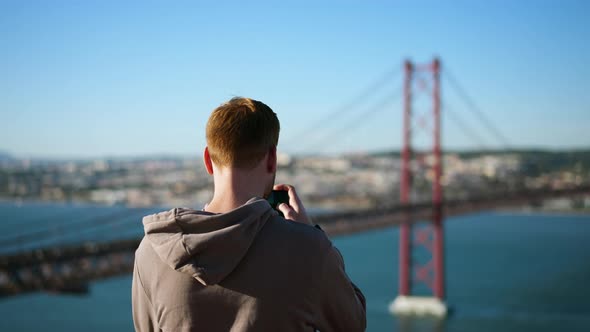 Traveling Male Tourist with Phone Films Landmark of Ponte 25 De Abril in Lisbon