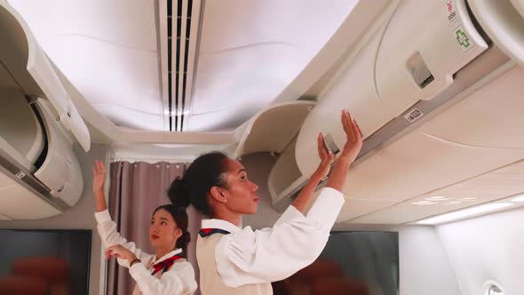 Two Beautiful flight attendants close luggage compartments overhead on aircraft.