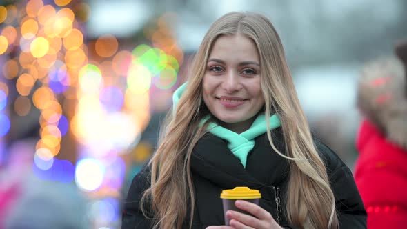 Young happy girl with cup of coffee in a New Year's decorated city.