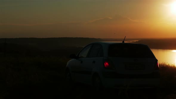 silhouette of couple waving their hands at the car at sunset