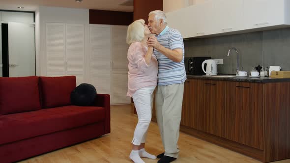 Happy Mature Senior Couple Dancing Laughing in Kitchen at Home, Celebrating Anniversary, Having Fun alt
