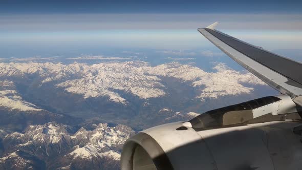 View From Above Through Airplane Window Flying Over Snowy Mountain Peaks At Daytime. aerial, POV alt