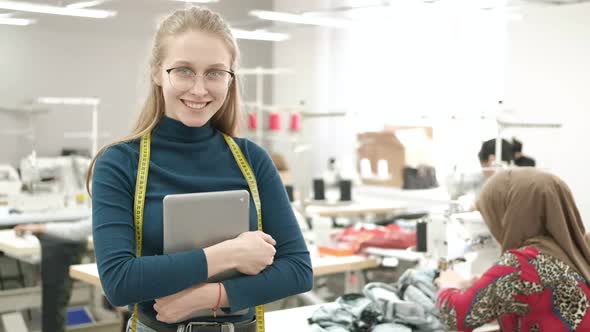 dressmaker in clothing factory among working seamstresses with tablet in hands alt