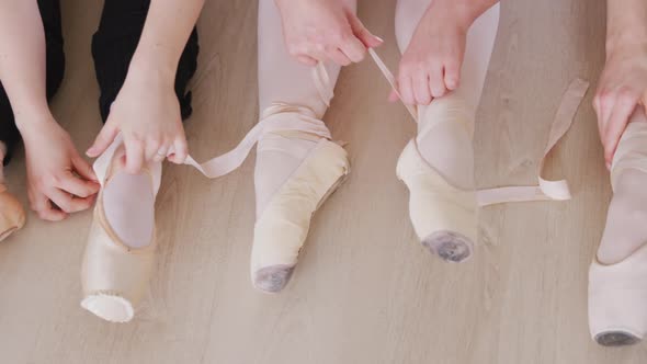Caucasian ballet female dancers sitting together on the floor and chatting while tying ballet shoes alt