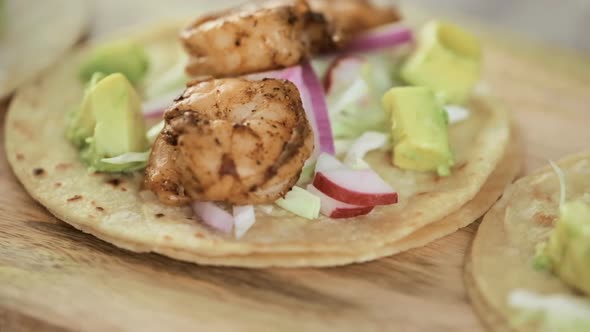 Preparing fresh chipotle shrimp tacos with cotija cheese on a white corn tortillas. alt