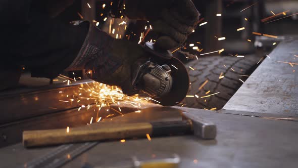 A Mechanic in an Auto Repair Shop with a Grinder Cuts Off a Metal Part Near the Wheel of a Car alt