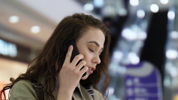 The Girl is Talking on the Phone Against the Background of the Escalator alt