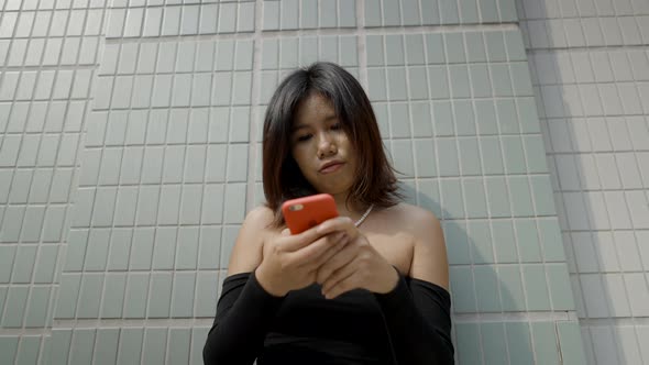 Asian Woman in Black Sexy Dress with Smartphone Standing Against Building Background alt