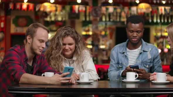 Group of Friends at a Bar Drinking Coffee and Discussing While Looking at the Screen of a Smartphone alt