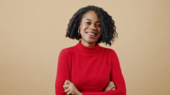 Young Confident African American Woman Laughing to Camera Posing with Folded Arms Over Beige Studio alt