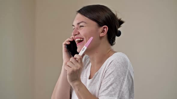 Happy Woman Holding Her Positive Result on Pregnancy Test and Talking By a Smartphone with the