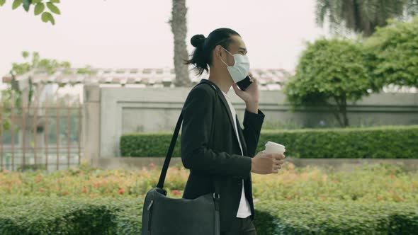 Asian businessman wearing a surgical mask and talk phone while walking on the street in the city.