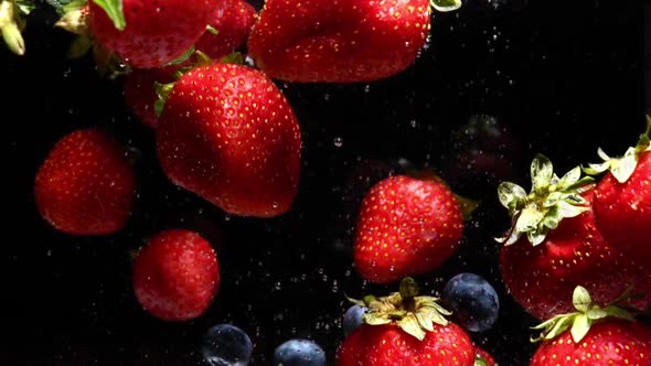 Slow Motion Drop of Blueberries and Strawberries Into Water on Black Background